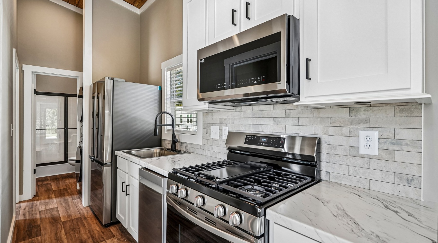 Kitchen interior detailing a stainless steel gas range, microwave, white upper cabinets, and marble-look countertops.